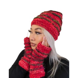 May include: A red knit hat and matching fingerless gloves. The hat and gloves have horizontal stripes of green, gold, and black. The knitwear is a warm, cozy accessory.
