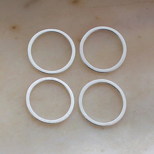 May include: Four silver jump rings, each with a circular shape, are arranged in a square pattern on a light beige surface.