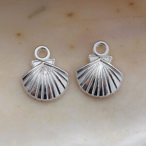 May include: Two silver-toned metal seashell charms with a loop at the top for attaching to jewelry or other crafts.
