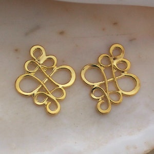 May include: Two gold-toned metal decorative charms in the shape of a stylized knot. The charms are intricate and have a delicate design.