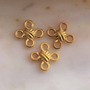 May include: Three gold-colored metal connector charms in the shape of a four-leaf clover. Each charm has a woven design.
