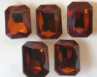 May include: Five dark brown, faceted, rectangular glass gems. The gems have a slightly orange hue.