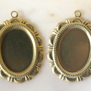 May include: Two antique brass-colored oval pendant trays with scalloped edges and a small loop at the top for attaching a chain. The trays have a recessed center for holding a photo or other small item. These are ideal for jewelry making.