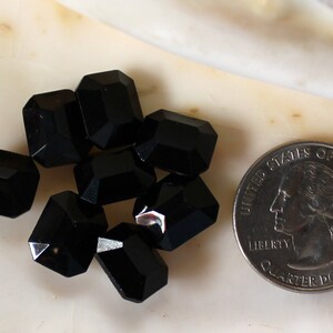 May include: A group of eight black faceted glass beads, each about the size of a quarter, arranged on a white surface.