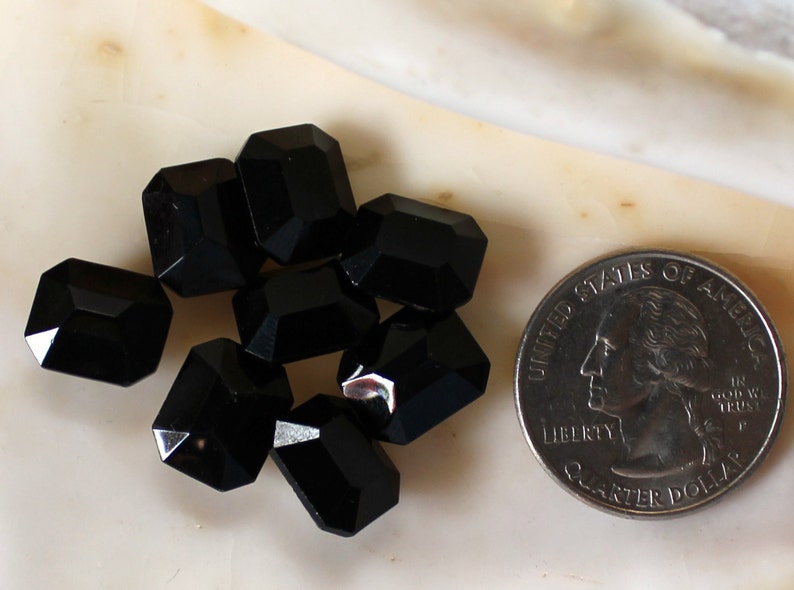 May include: A group of eight black faceted glass beads, each about the size of a quarter, arranged on a white surface.