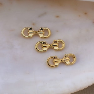May include: Three gold-toned metal bow-shaped connector charms. The charms are designed to be used in jewelry making.