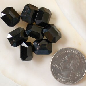May include: A group of seven black faceted glass beads, each about the size of a US quarter.