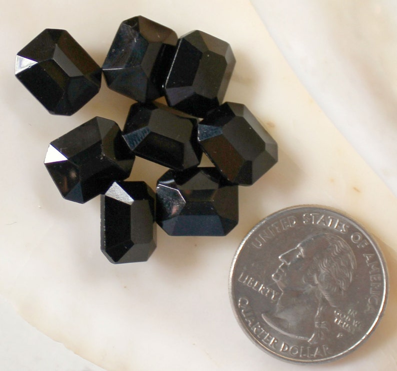 May include: A group of seven black faceted glass beads, each about the size of a US quarter.