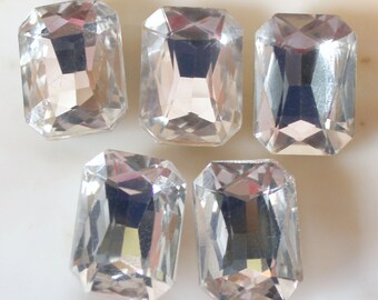 May include: Five clear glass emerald-shaped rhinestones. The rhinestones are faceted and have a high shine.