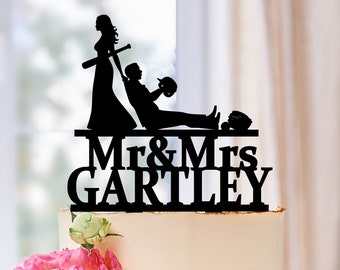 May include: Black silhouette cake topper of a bride and groom with a baseball theme. The bride is holding a baseball bat and the groom is lying on the ground with a baseball glove and ball. The text "Mr & Mrs Gartley" is below the couple.