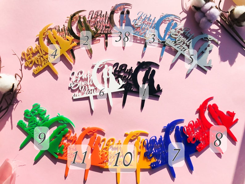 May include: Assortment of 11 acrylic cake toppers in various colors, featuring a crescent moon design with the text "I Put a Spell on You".