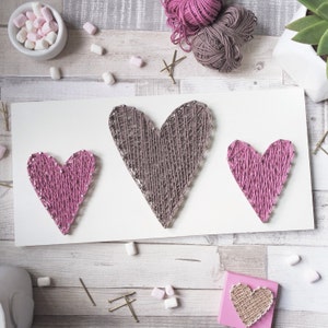 Könnte beinhalten: Drei String Art Herzen auf weißem Hintergrund. Das größte Herz ist braun, das mittlere Herz ist rosa und das kleinste Herz ist rosa.
