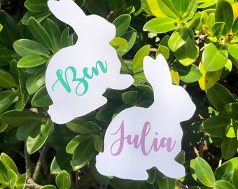 May include: Two white bunny-shaped place cards with the names "Ben" and "Julia" written in green and purple lettering.