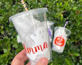 May include: A clear plastic cup with a white ghost and the name "Emma" in red lettering. The cup has a black and white striped straw and is filled with white tissue paper.