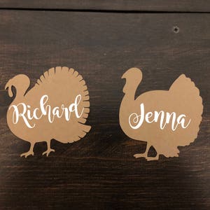 Puede incluir: Dos tarjetas de lugar de pavo de papel marr&oacute;n con los nombres "Richard" y "Jenna" escritos en blanco.