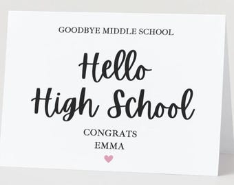 May include: A white greeting card with the text "Goodbye Middle School" and "Hello High School" in a black script font. The card also includes "Congrats Emma" and a small pink heart.