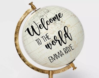 May include: A white globe with a gold stand and a black inscription that reads "Welcome to the world Emma Raye".