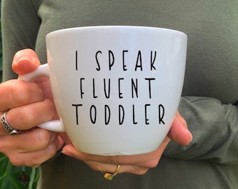 May include: White ceramic mug with black text that reads "I speak fluent toddler".
