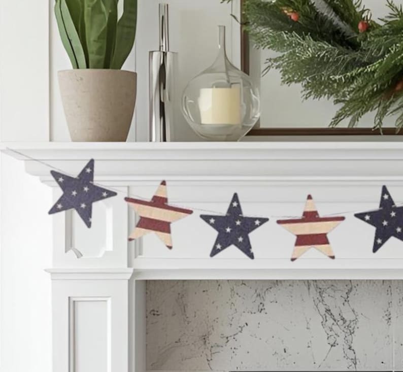 May include: A decorative garland featuring alternating star-shaped cutouts. The stars display patterns of dark blue with white stars and red and white horizontal stripes, strung together on a thin cord and displayed across a white fireplace mantel.