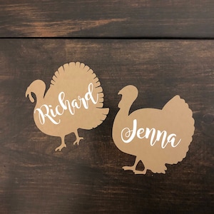 Puede incluir: Dos recortes de tarjetas de lugar de pavo de papel marr&oacute;n con los nombres Richard y Jenna escritos en blanco.