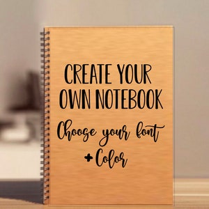 May include: A spiral-bound notebook with a light brown cover. The text "CREATE YOUR OWN NOTEBOOK" is printed in a bold, black font. Below, the text "Choose your font + Color" is written in a cursive font.