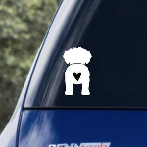 May include: White silhouette of a dog with a heart on its rear end. The dog is facing away from the viewer. The silhouette is on a black background.