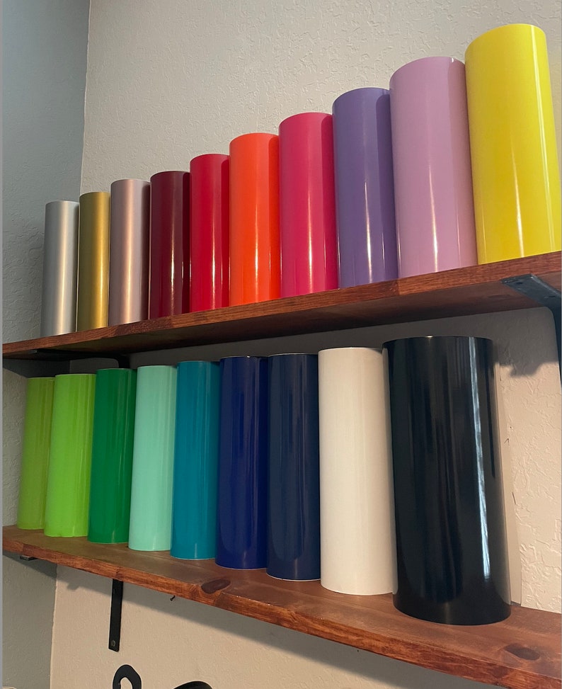 May include: A collection of vinyl rolls in various colors, including gold, silver, red, orange, pink, purple, yellow, green, blue, white, and black. The rolls are arranged on two wooden shelves.