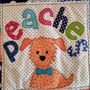 May include: A white and blue polka dot fabric square with the word "Peaches" in colourful letters and a brown and orange dog with a blue bow tie.