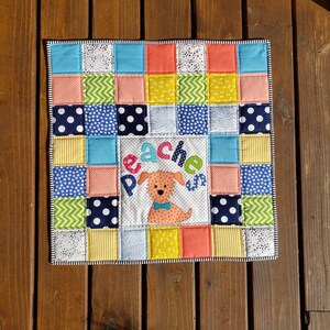 May include: A colourful patchwork quilt with a dog and the word "Pache's" in the centre. The quilt is made of various fabrics in shades of blue, green, yellow, pink, and white.