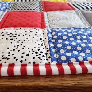 May include: A patchwork quilt featuring a red, white and blue colour scheme. The quilt is made from different fabrics with various patterns, including polka dots, stripes and geometric designs. The quilt has a red and white striped border.