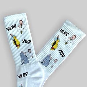 May include: White socks with a repeated pattern of a man in a white shirt and tie, holding a yellow rubber ducky. The text "Live Fast Die Old" and "I Prefer a Flan" are also repeated on the socks.