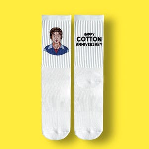 May include: A pair of white socks with a cartoon image of a person on one sock and the text "Happy Cotton Anniversary" on the other sock.