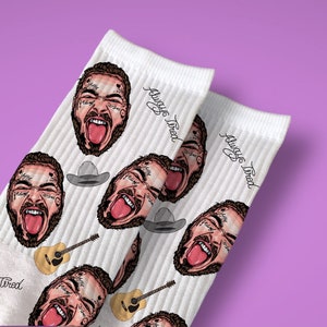 May include: White socks with a repeating pattern of a cartoon face with a tongue sticking out, a cowboy hat, and a guitar. The text "Always Tired" is repeated on the socks.