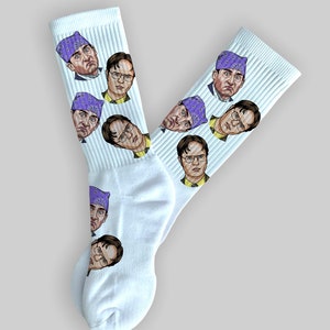 May include: A pair of white socks with a repeating pattern of a man's face wearing a purple bandana. The man's face is depicted in a cartoon style.