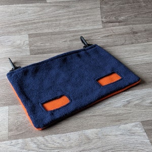 May include: A blue fleece hammock with two orange fleece openings. The hammock has two black clips on the top.