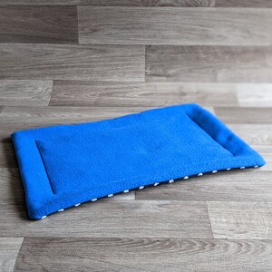 May include: A blue fleece pet bed with white polka dots on the border. The bed is lying flat on a wood floor.