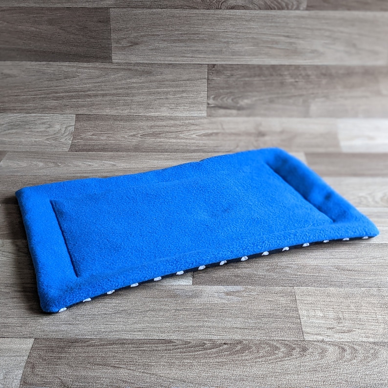 May include: A blue fleece pet bed with white polka dots on the border. The bed is lying flat on a wood floor.