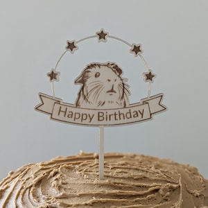May include: Wooden cake topper with a guinea pig illustration and the text "Happy Birthday" in a banner. The topper is decorated with stars.