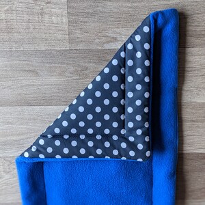 May include: A blue fleece pet bed with a black and white polka dot fabric lining. The bed is folded in half, showing the lining.