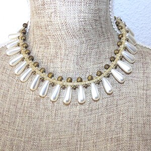 Kurze Halskette im Cleopatra-Stil an Leinenfaden mit langen, weißen, perlenartigen, tropfenförmigen Perlen.