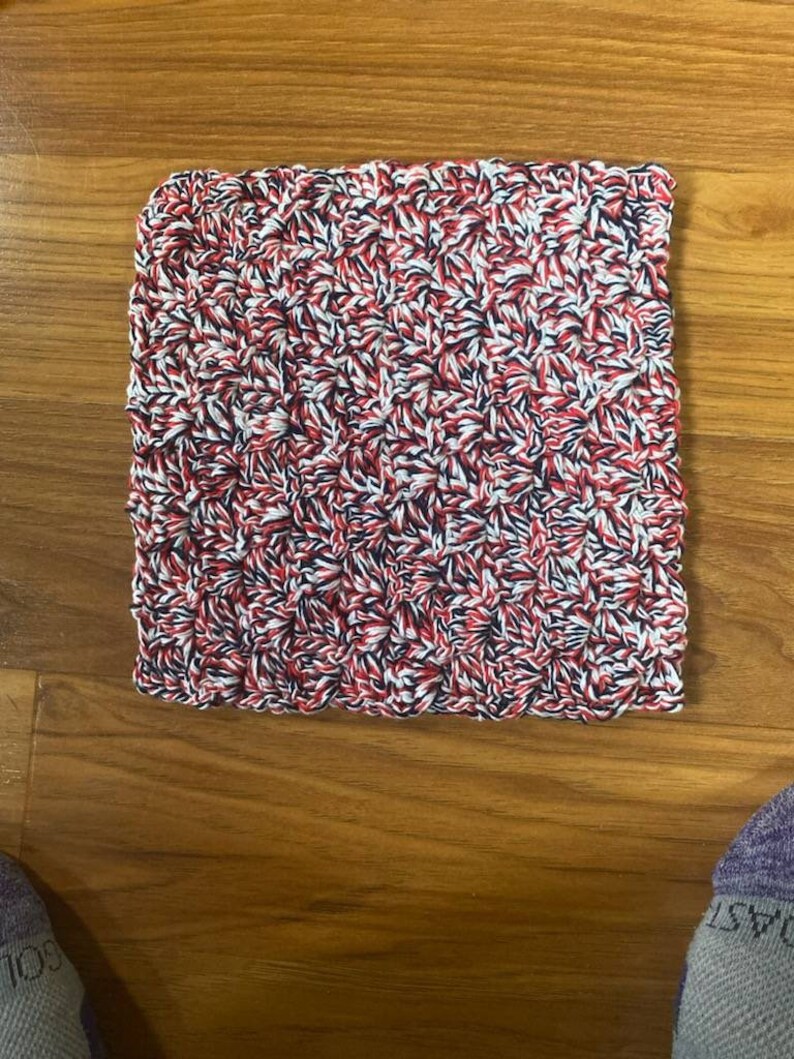 May include: A red, white, and blue knitted dishcloth. The dishcloth is made with a textured pattern.