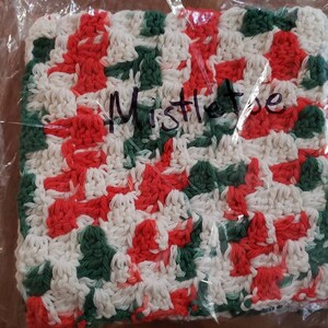 May include: A white, red, and green crocheted dishcloth with the word "Mistletoe" written on it.