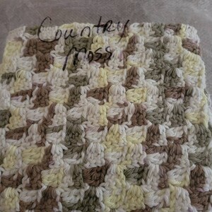 May include: A crocheted square with a country moss design in shades of white, yellow, brown, and green. The square is in a plastic bag with the words "Country Moss" written on it.