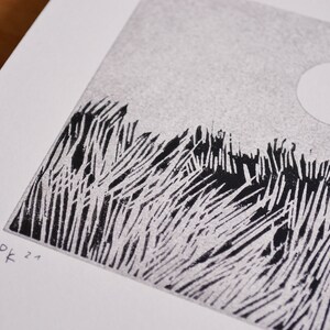 May include: A black and white linocut print on white paper featuring a textured field of tall grass under a circular sun. The artwork displays a stippled sky and bold, vertical ink strokes for the vegetation. The initials Pk and 21 are printed.
