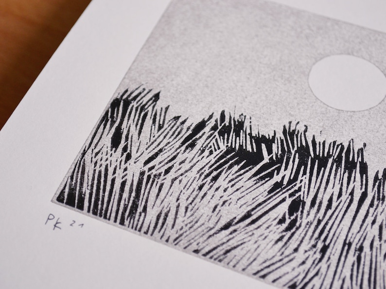 May include: A black and white linocut print on white paper featuring a textured field of tall grass under a circular sun. The artwork displays a stippled sky and bold, vertical ink strokes for the vegetation. The initials Pk and 21 are printed.