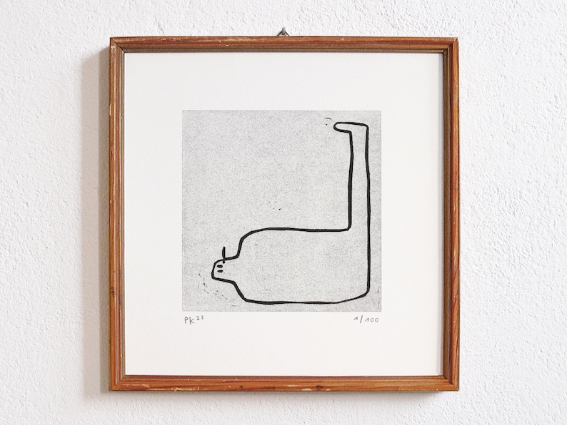 May include: A framed black and white line drawing of a stylized figure with a long neck and a rounded body. The drawing is on a textured paper background. The frame is made of wood and has a light brown finish. The drawing is signed "PK 22" and numbered "1/400".
