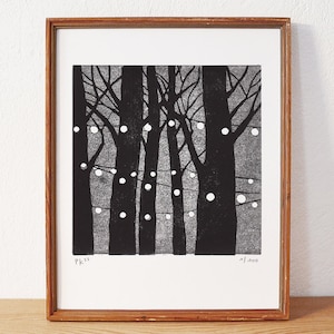 May include: A framed monochrome print depicting trees adorned with fairy lights. The artwork shows a forest scene with tall, dark trees and spherical lights strung between them. The frame is made of wood.