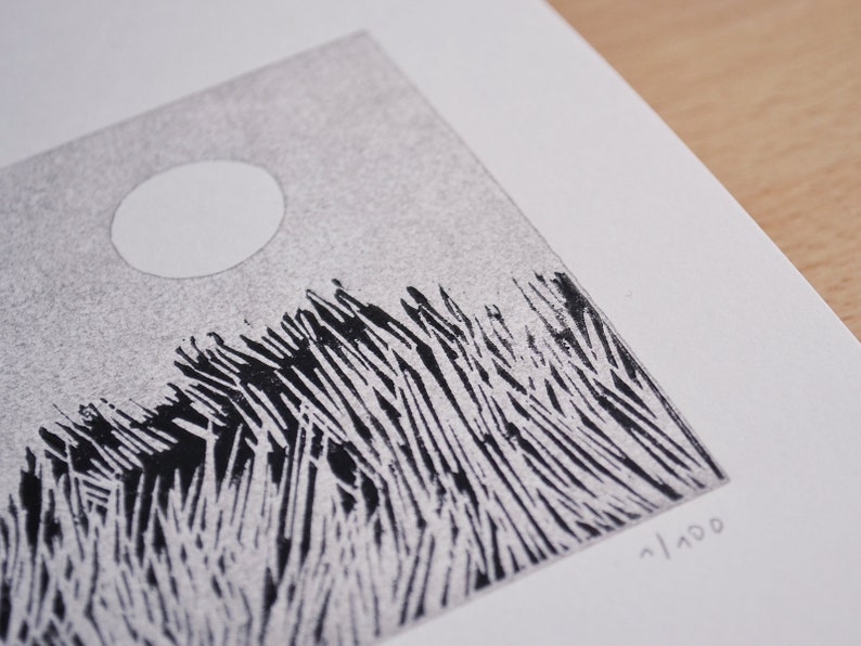 May include: A black and white linocut print on textured paper featuring a stylised landscape with tall, sharp grass blades and a solid white circular moon in a stippled grey sky. The print is numbered 1/100 in the bottom right corner.