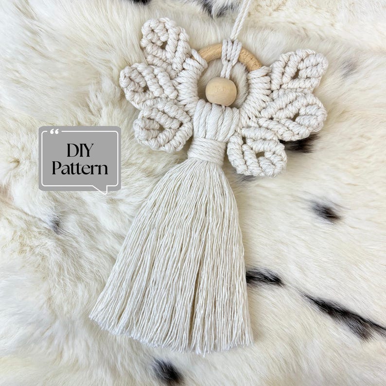 Handmade macramé angel ornament with braided wings and a long tassel body, shown on soft fur with a ‘DIY Pattern’ label.