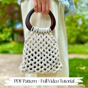 May include: A beige macrame handbag with a dark brown wooden handle. The bag is held up by a person. The text "PDF Pattern + Full Video Tutorial" is at the bottom of the image.